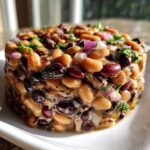 A molded serving of Dense Bean Salad featuring mixed beans, red onion, and herbs, glistening with dressing.