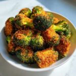 A close-up of vibrant green Parmesan Crusted Broccoli Florets piled high in a white serving bowl.