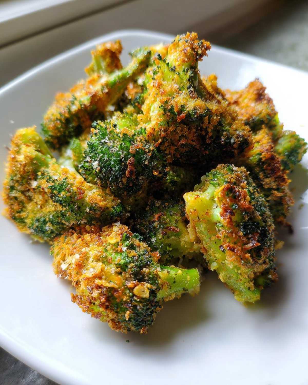 A close-up of crispy, golden Parmesan Crusted Broccoli Florets piled on a white plate.