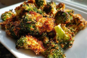 Close-up of golden brown Parmesan Crusted Broccoli Florets piled on a white plate, beautifully roasted.
