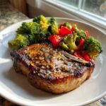 A perfectly cooked Sheet Pan Lemon Garlic Pork Chops glazed with garlic sauce, served with bright green broccoli and red peppers.
