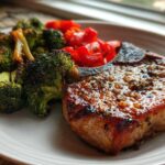 A perfectly cooked Sheet Pan Lemon Garlic Pork Chop, glazed and served with roasted broccoli and red peppers.