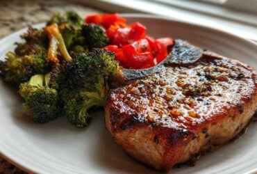 A perfectly cooked Sheet Pan Lemon Garlic Pork Chop, glazed and served with roasted broccoli and red peppers.