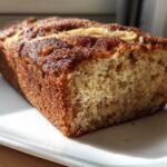 A close-up view of a freshly baked Snickerdoodle Banana Bread loaf with a dark, sugary crust, showing the moist crumb texture.