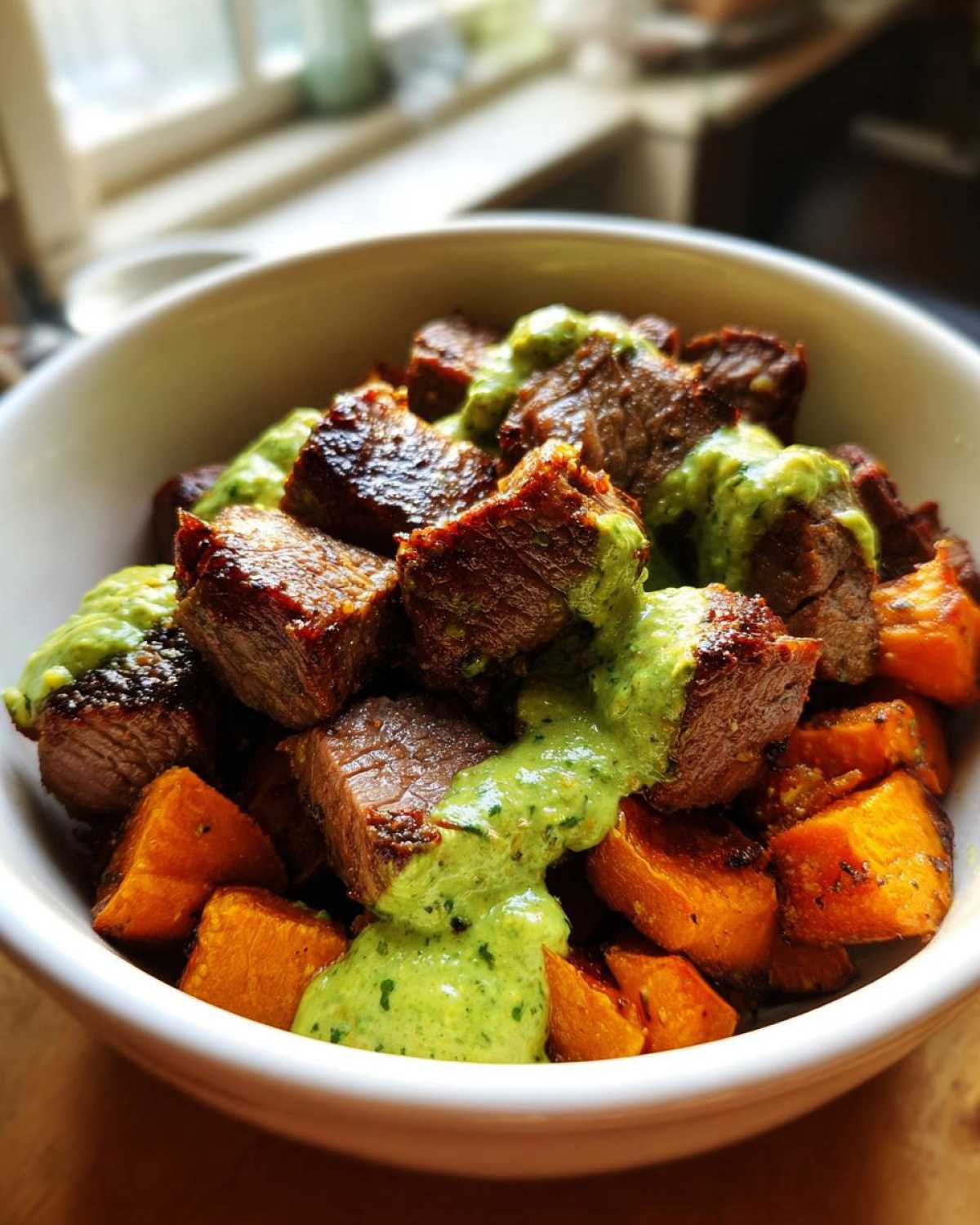 Close-up of Steak and Sweet Potato Bowls topped generously with bright green Avocado-Cilantro Drizzle.
