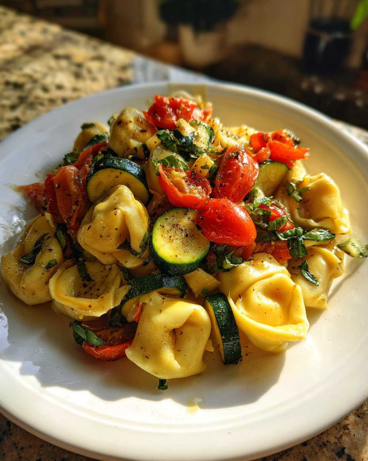 A close-up of Tortellini with Summer Veggies, featuring pasta mixed with sliced zucchini and halved cherry tomatoes.